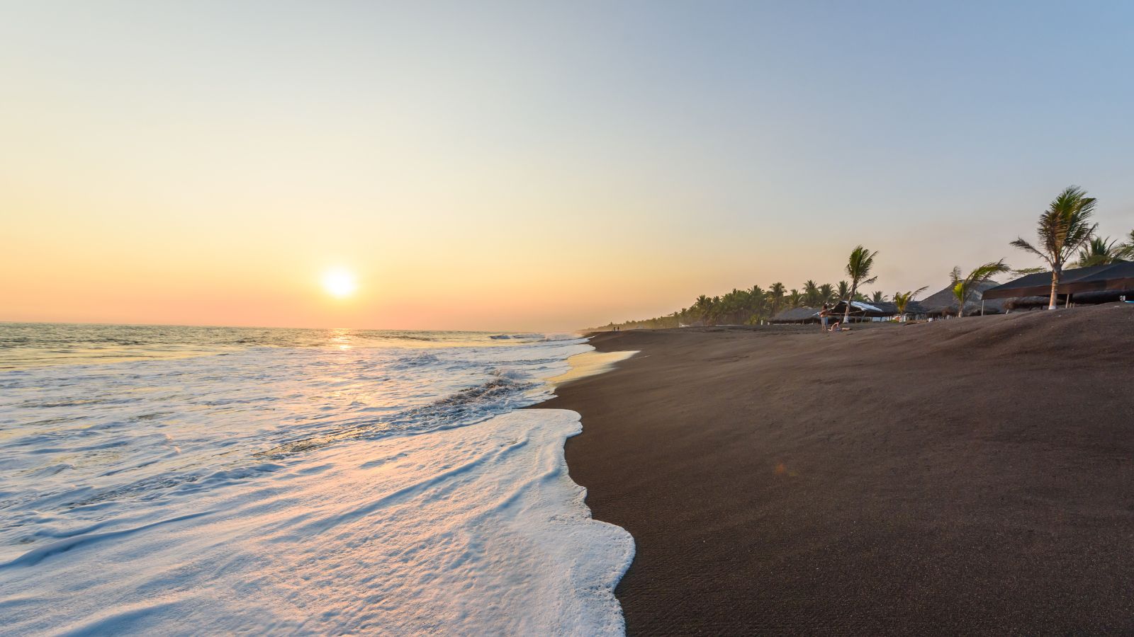 Sunset over a black-sand beach in Guatemala with waves rolling toward the shore